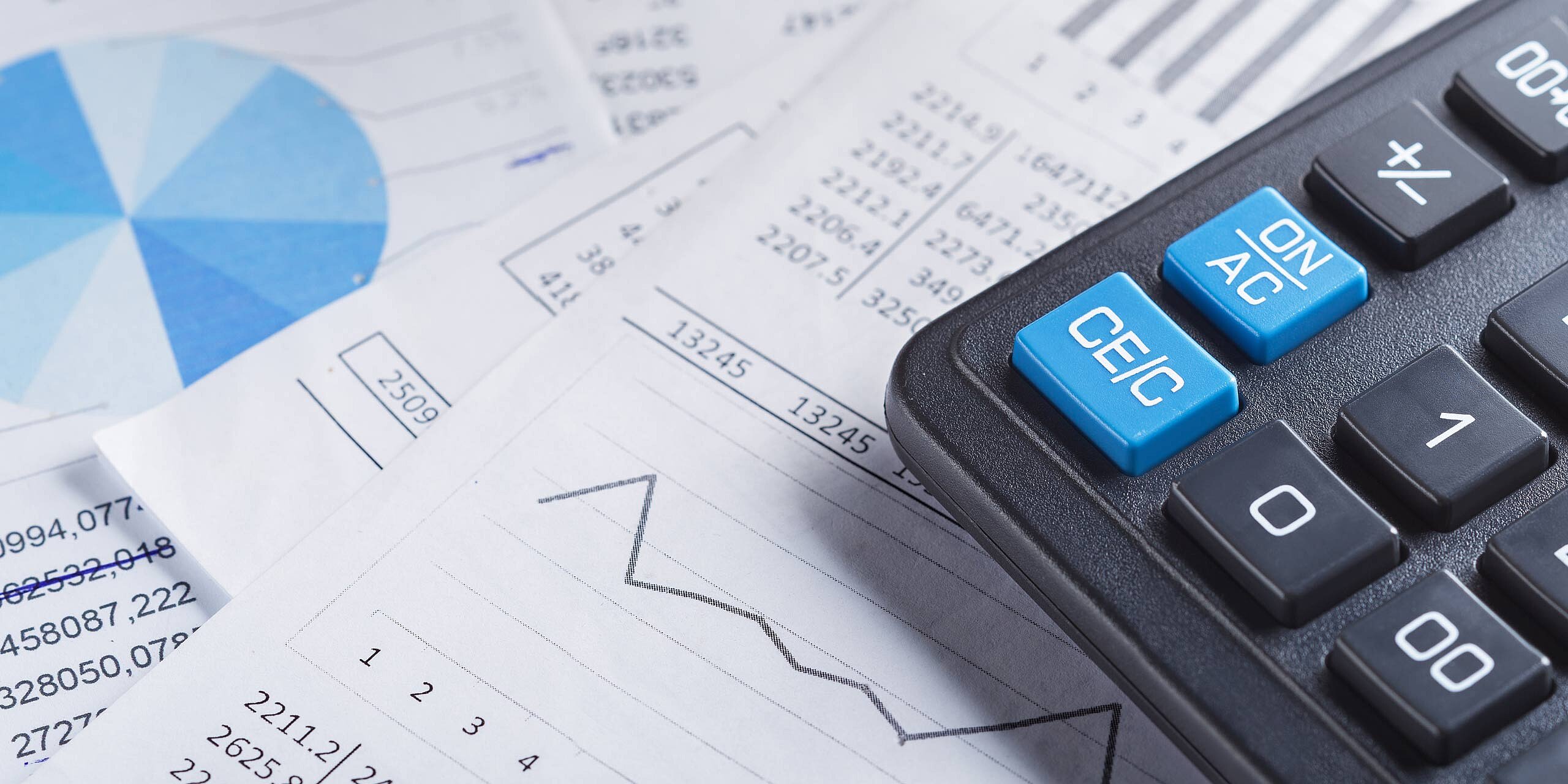 Eine Nahaufnahme eines schwarzen Taschenrechners auf Finanzdokumenten. Die Dokumente zeigen Diagramme und Grafiken, darunter ein blaues Kreisdiagramm und ein Liniendiagramm. Der Taschenrechner verfügt über große blaue Tasten mit der Aufschrift „ON“ und „CE/C“.